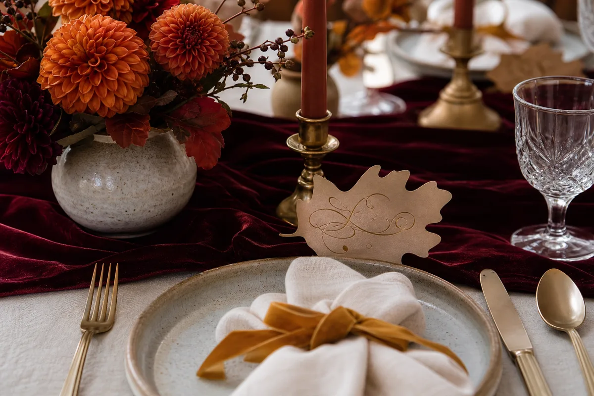 Table de mariage automnale avec chemin de table bordeaux, bougies et dahlias terracotta