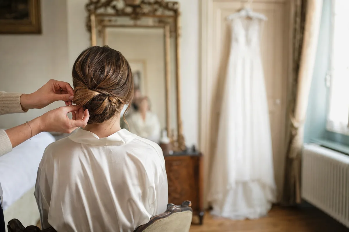 Mariée en peignoir face au miroir pendant la coiffure, lumière du matin